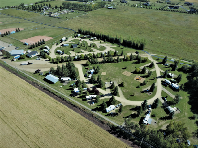 Aerial view of campground with RVs, cabins, trees, and winding roads on farmland.