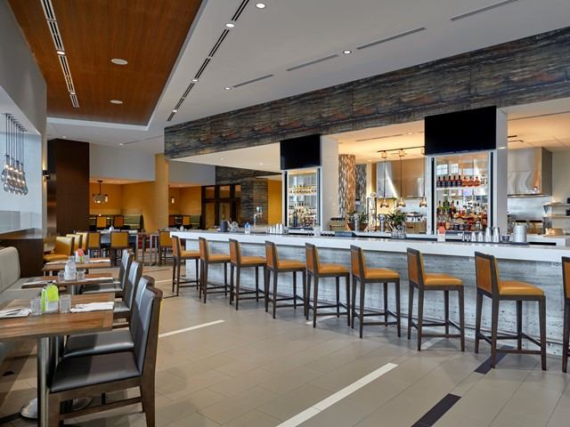 Modern hotel bar with high chairs, stocked shelves, and dining tables.