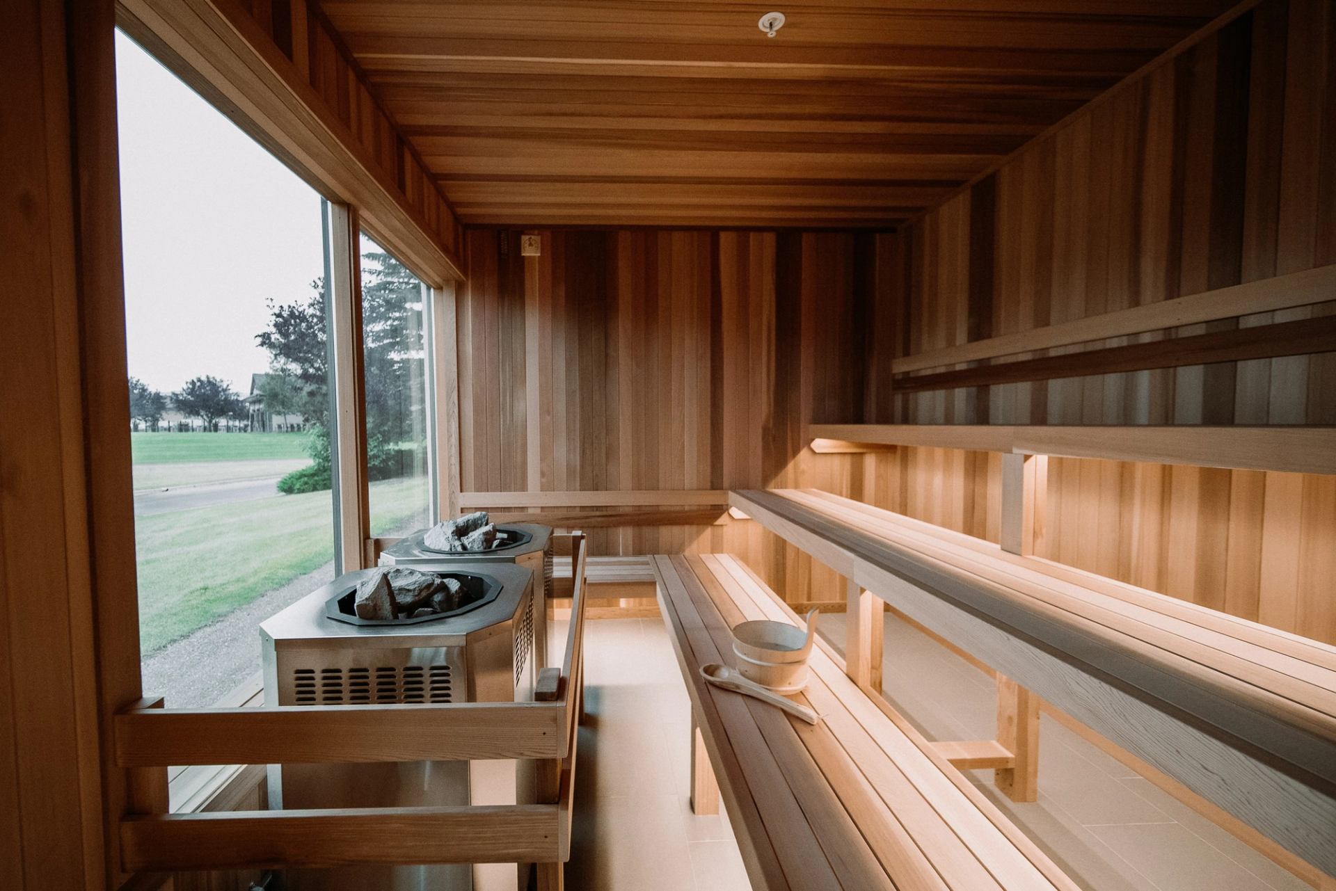 Tiered wooden sauna with heaters and a large window overlooking nature.