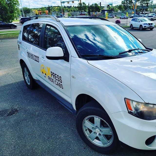 White Xpress Ride Cabs SUV with logo, parked near other vehicles and trees.
