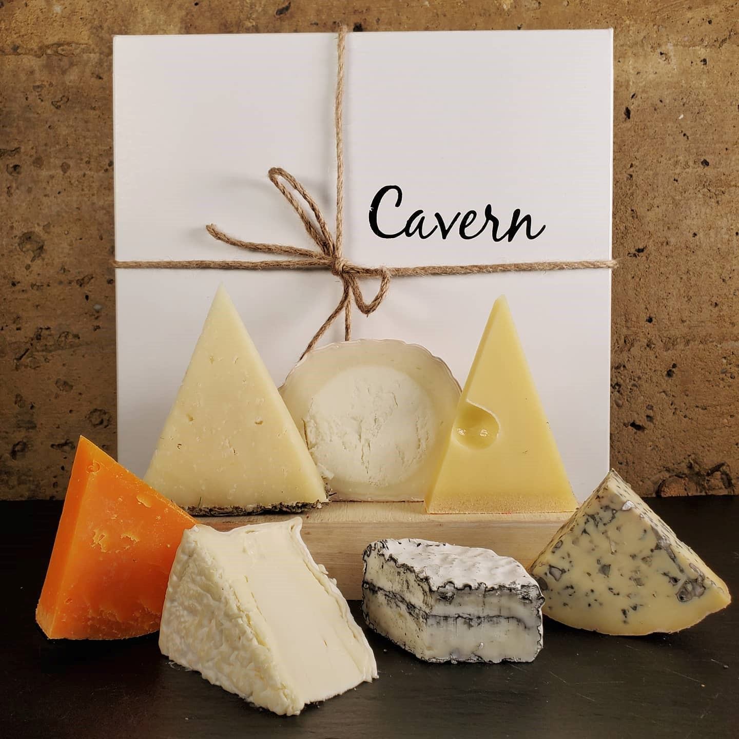 Assorted cheeses in front of a white Cavern box tied with string.