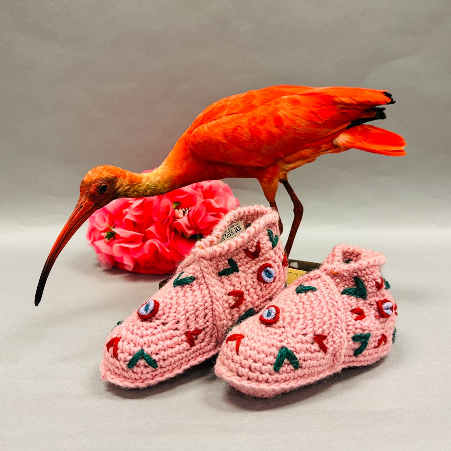A scarlet ibis, a pink flower, and two pink crocheted booties with colorful embroidery.