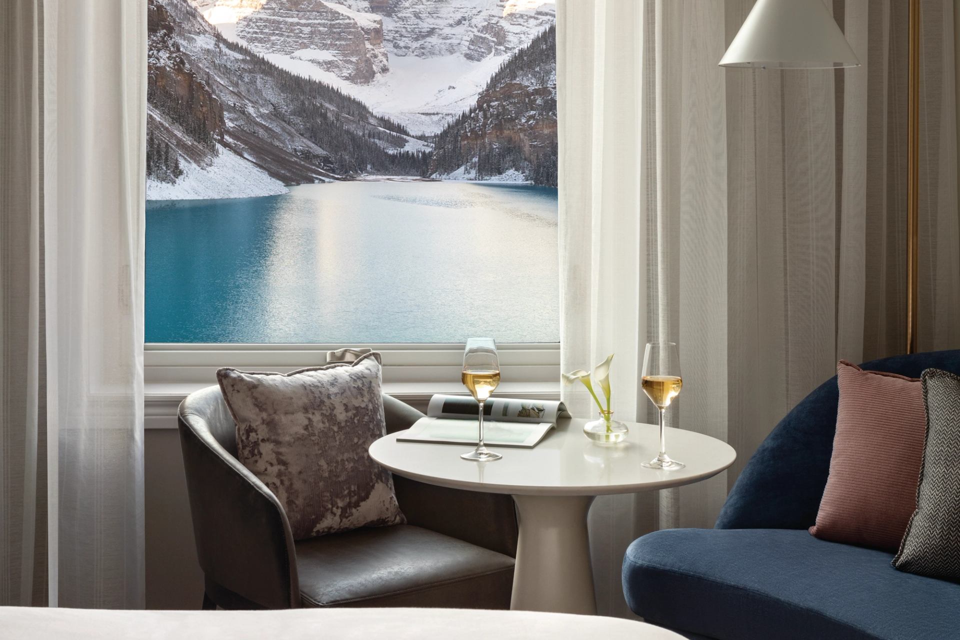 Hotel sitting area with wine glasses, lake and snow-covered mountains visible through window.