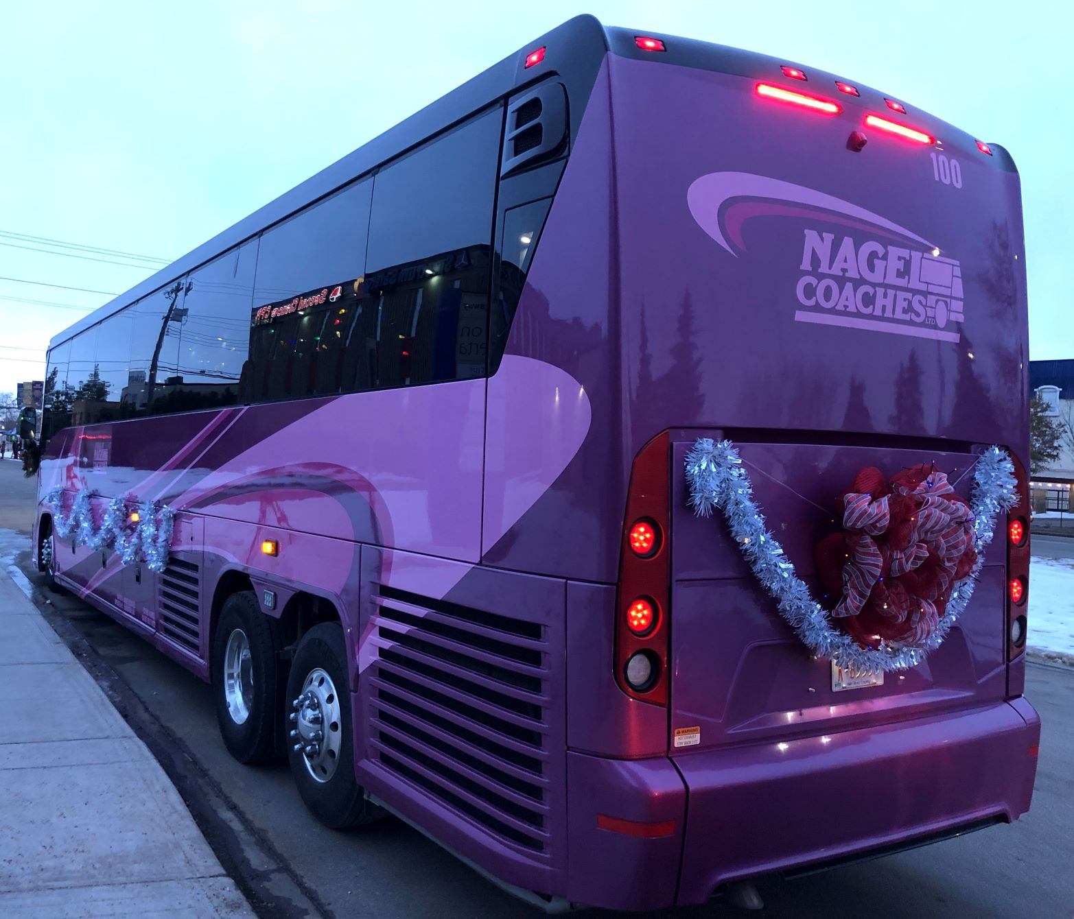 Nagel Coaches motorcoach decorated with holiday garland and lights at a city curb.