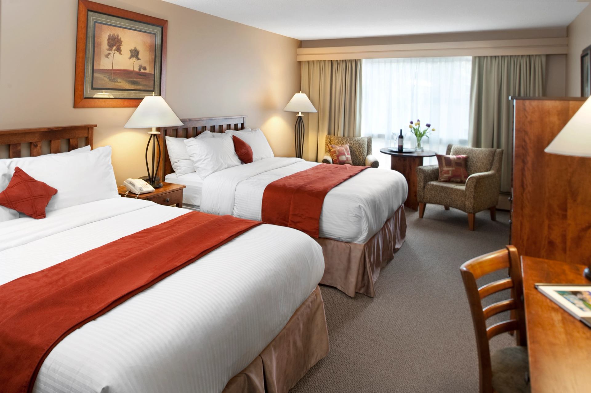 Hotel room with two queen beds, red runners, and cozy seating area