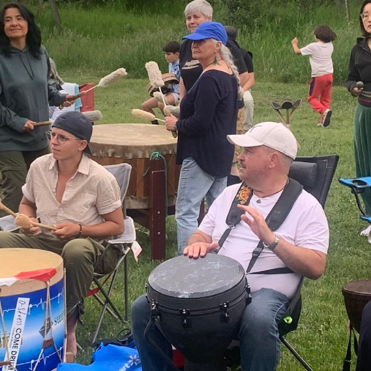 Group of people seated outdoors playing hand drums together on grass during a Circles of Rhythm gathering.