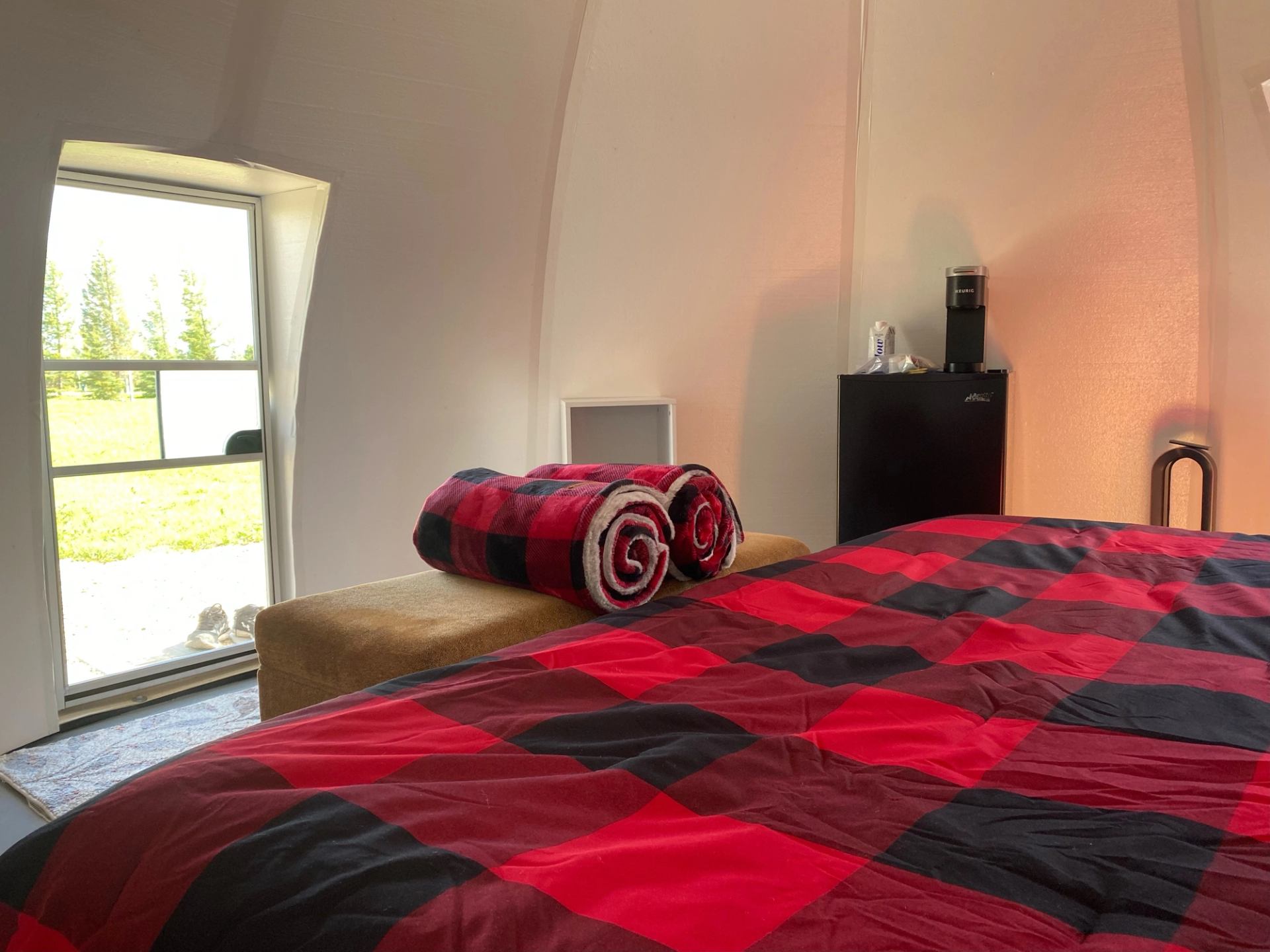 Dome room with plaid bedding, ottoman, and coffee station near window.