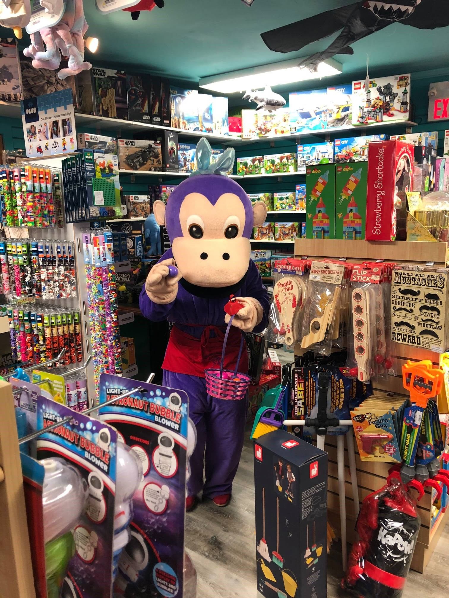 Toy store aisle with shelves of games and a plush character in front of displays.