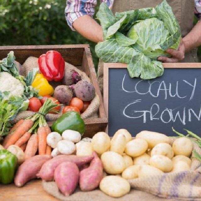 Farmers market produce table with chalkboard reading “Local Grown” and vegetables, including onions.