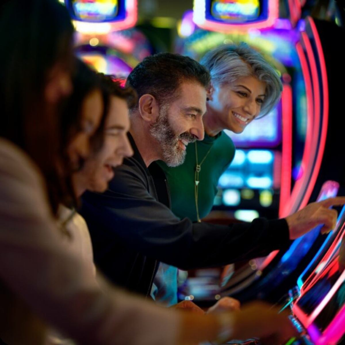 People play brightly lit slot machines in a casino, touching screens and buttons.