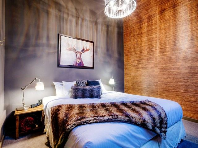 Bedroom with white bed, fur throw, moose artwork, bedside lamps and wood accent wall.