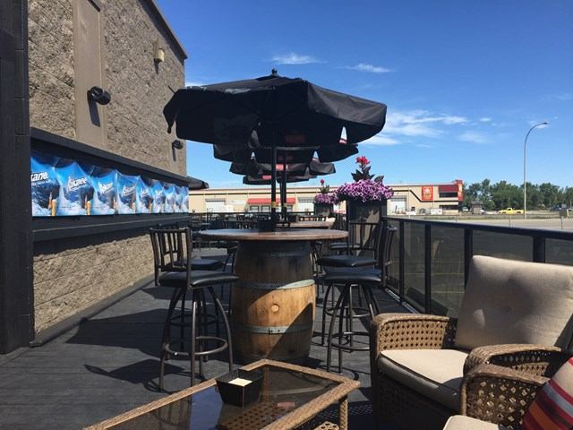 Outdoor patio with a barrel table and umbrellas, surrounded by chairs and a scenic view.