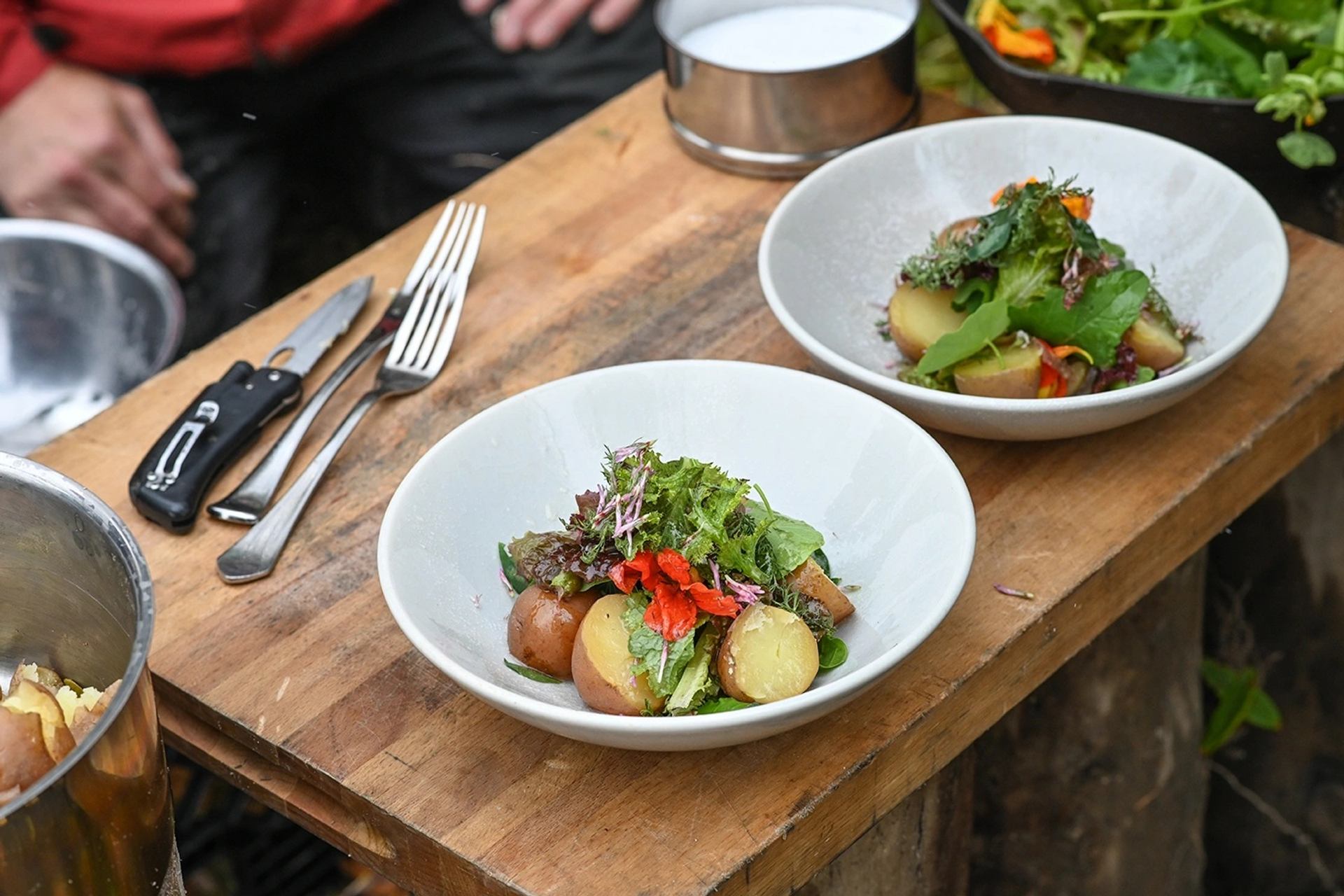 Two white bowls of potato salad with mixed greens on a rustic wooden table.