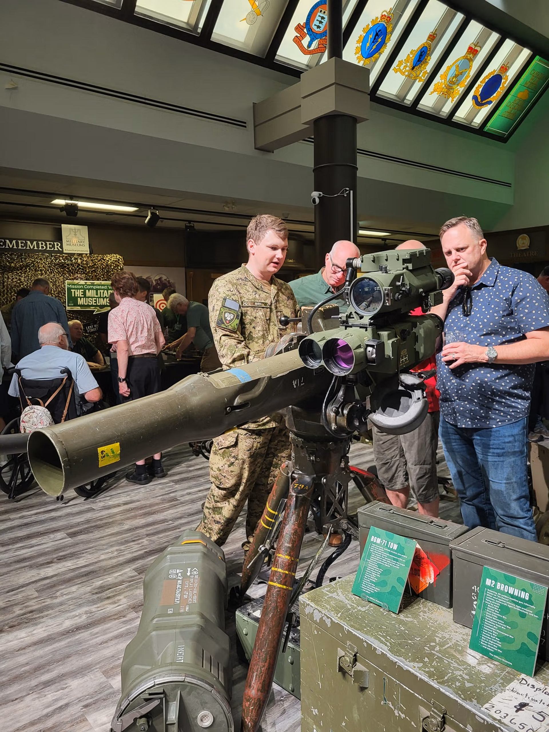 Three men, one in military uniform, observe a missile launcher on display at a museum.