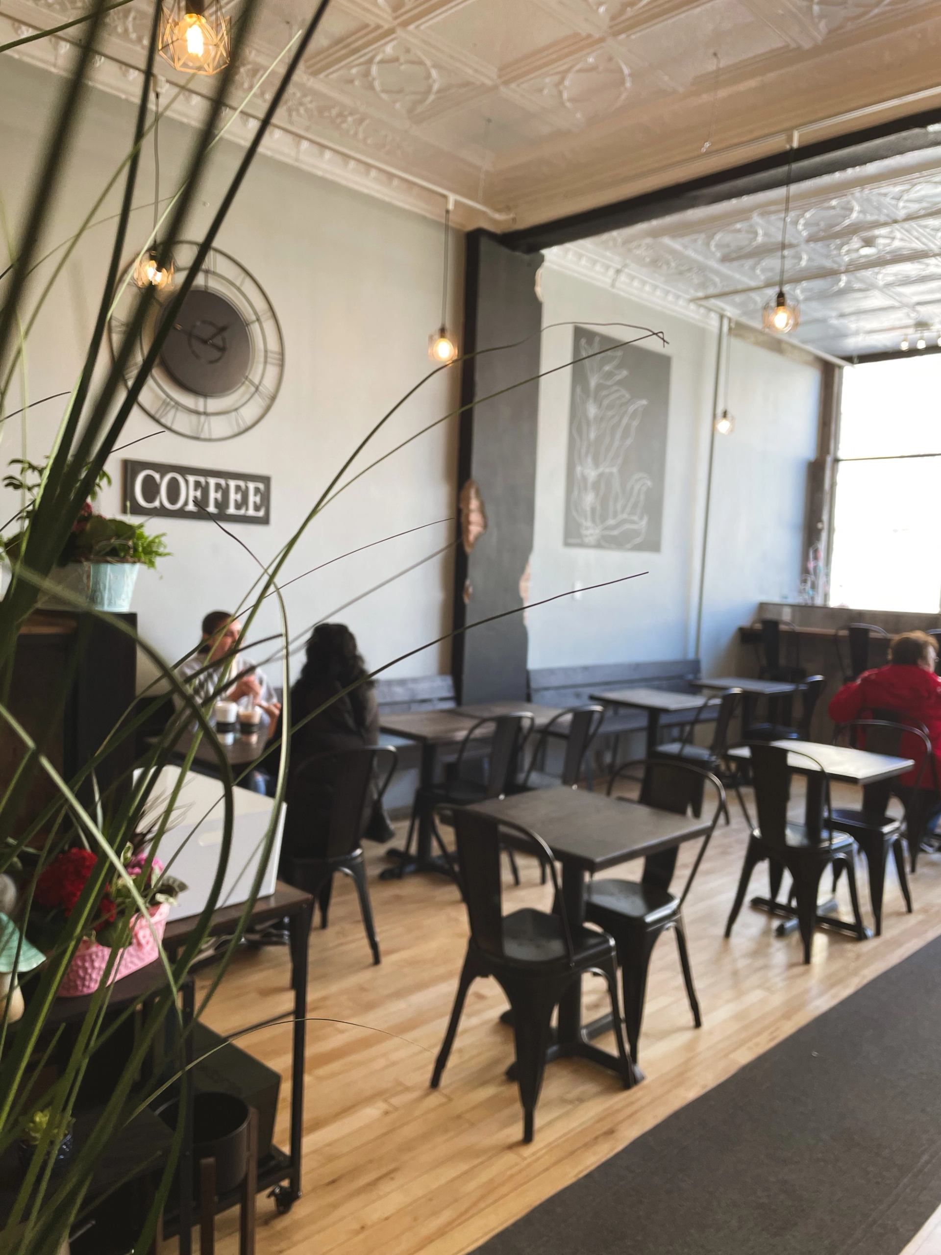 Small coffee shop interior with metal tables, hanging lights and a few seated customers.