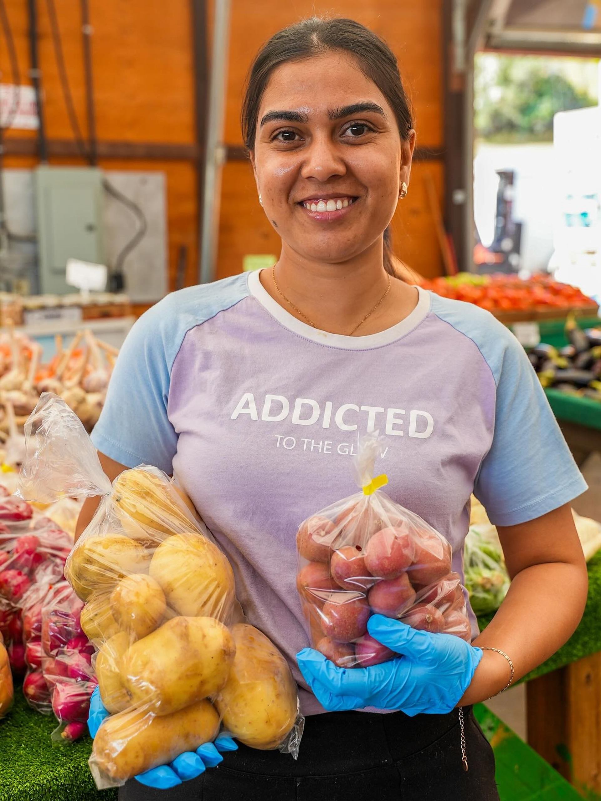 Person holding bags of potatoes and tomatoes at a produce stand in Crossroads Market.