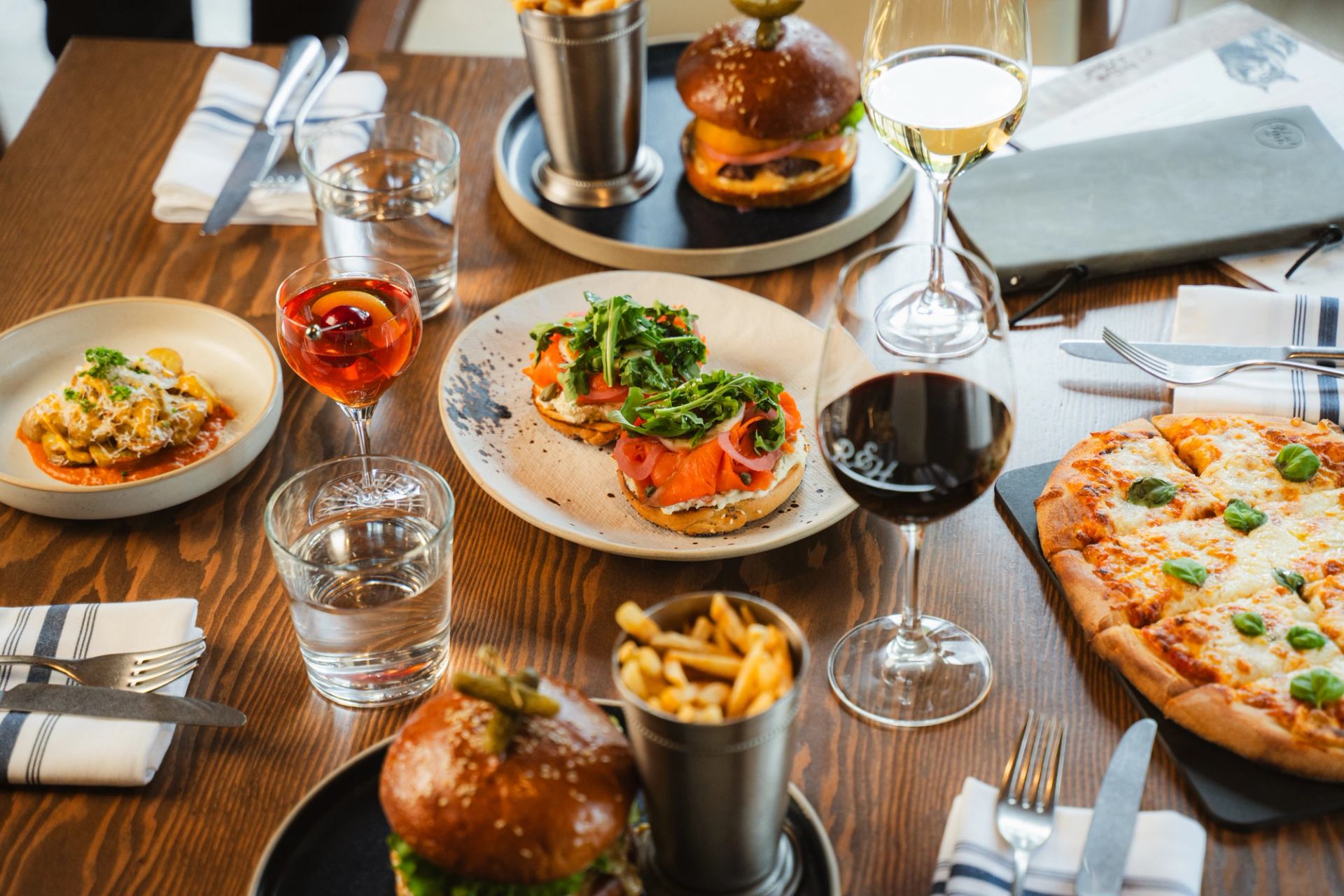 Table with gourmet burgers, pizza, fries, and wine at Everwild Canmore restaurant.
