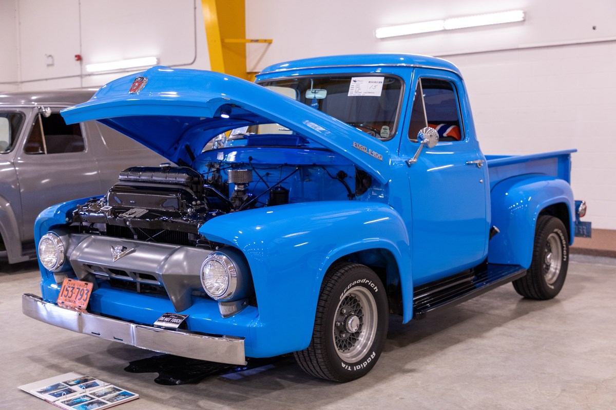 A bright blue vintage Ford F-100 pickup truck with its hood open, revealing the engine.