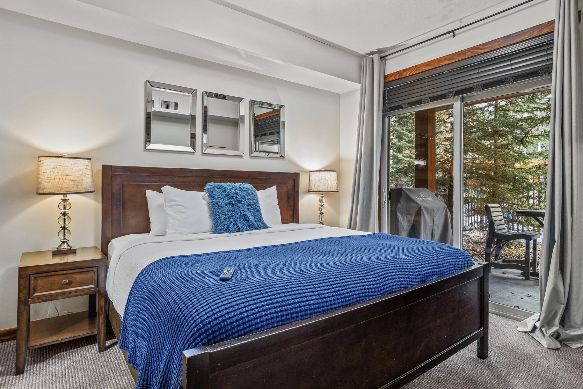 Bedroom with wooden bed, blue blanket, bedside lamps and patio doors to balcony.