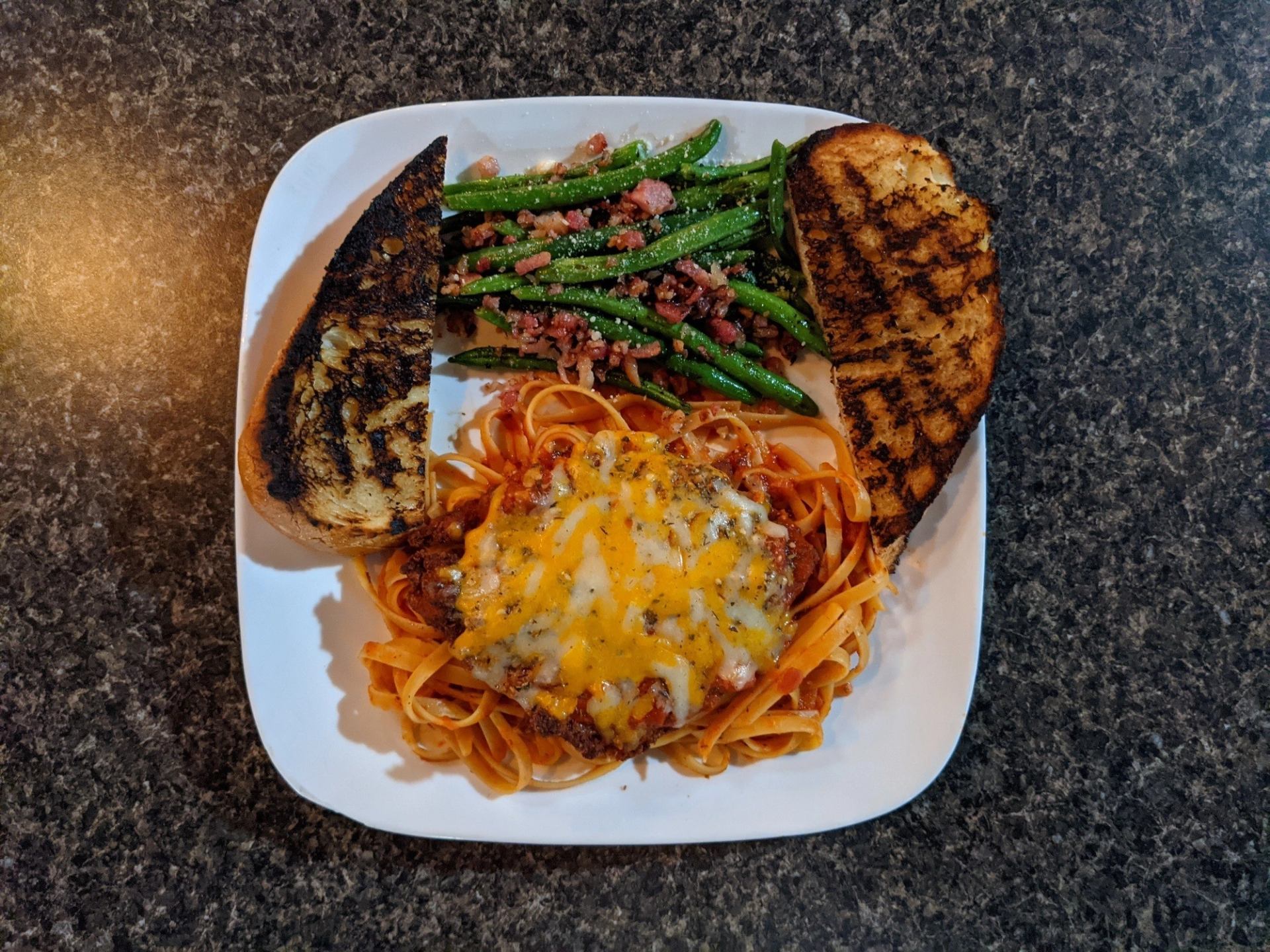 White plate with cheesy pasta, grilled garlic bread, and green beans topped with bacon.