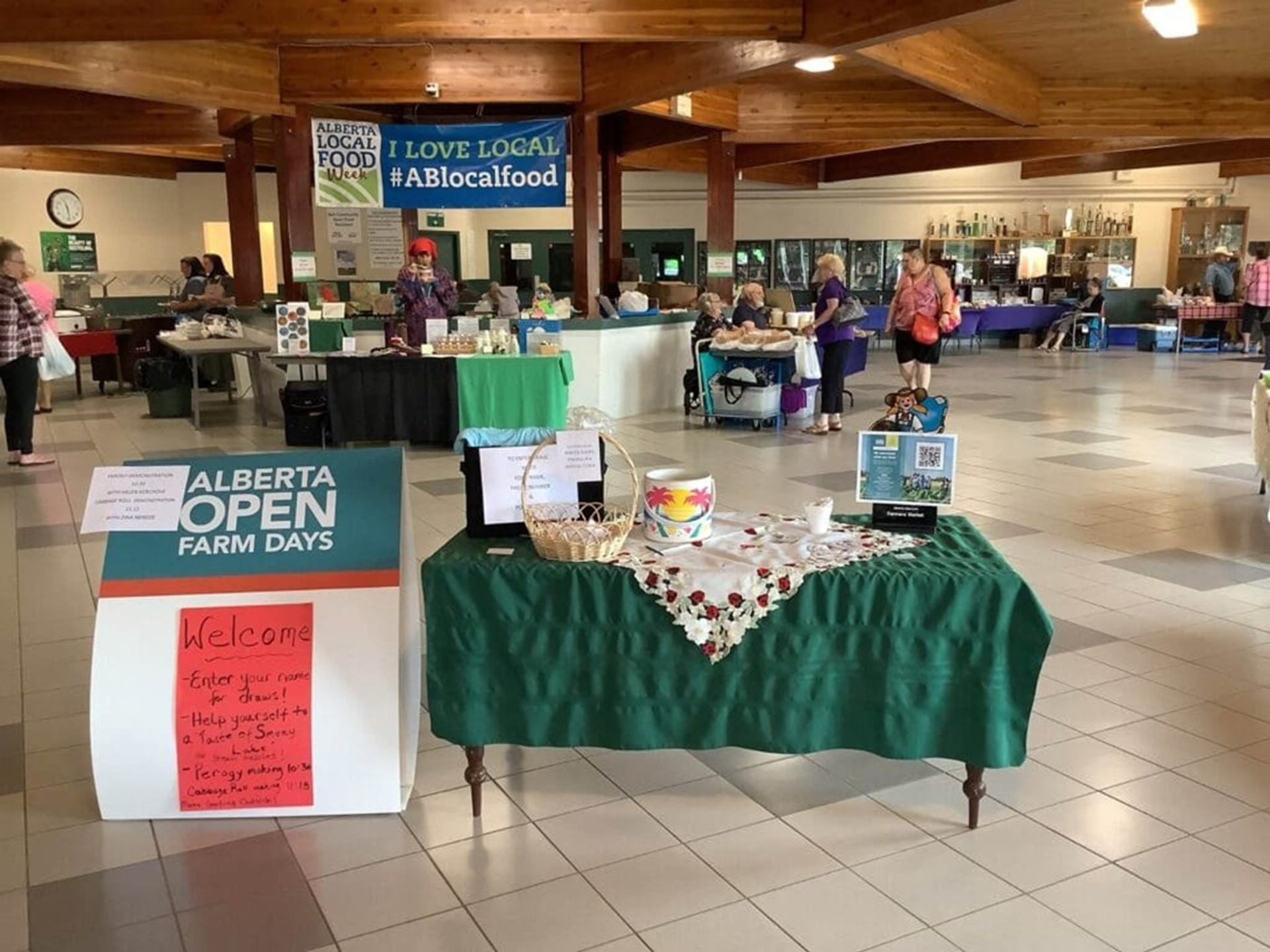 Indoor Alberta Open Farm Days market with vendor tables, welcome sign and visitors browsing.