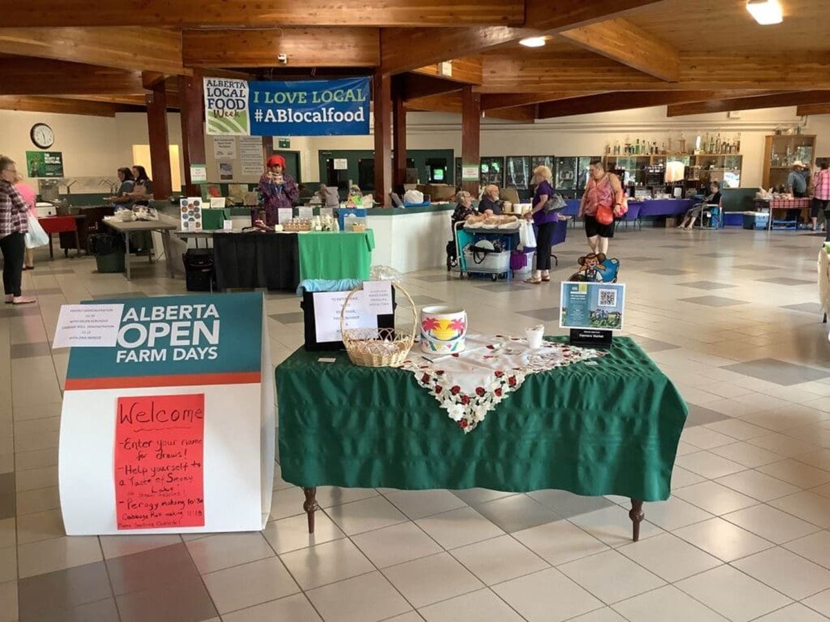 Indoor Alberta Open Farm Days market with vendor tables, welcome sign and visitors browsing.
