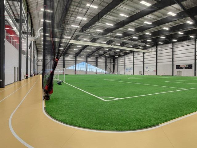 Indoor turf field beside running track, netted wall and high ceiling lights.