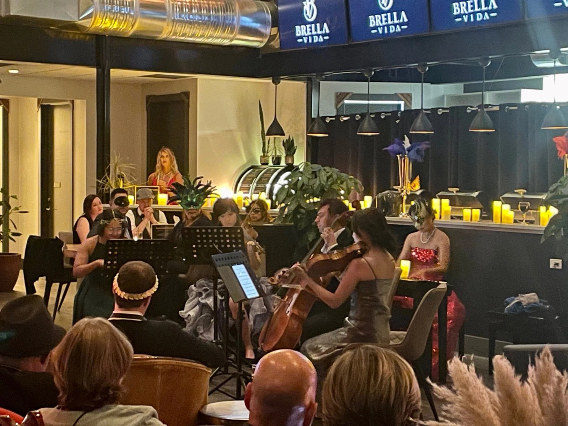 Musicians in formal wear perform for seated audience at candlelit Brella Vida venue.
