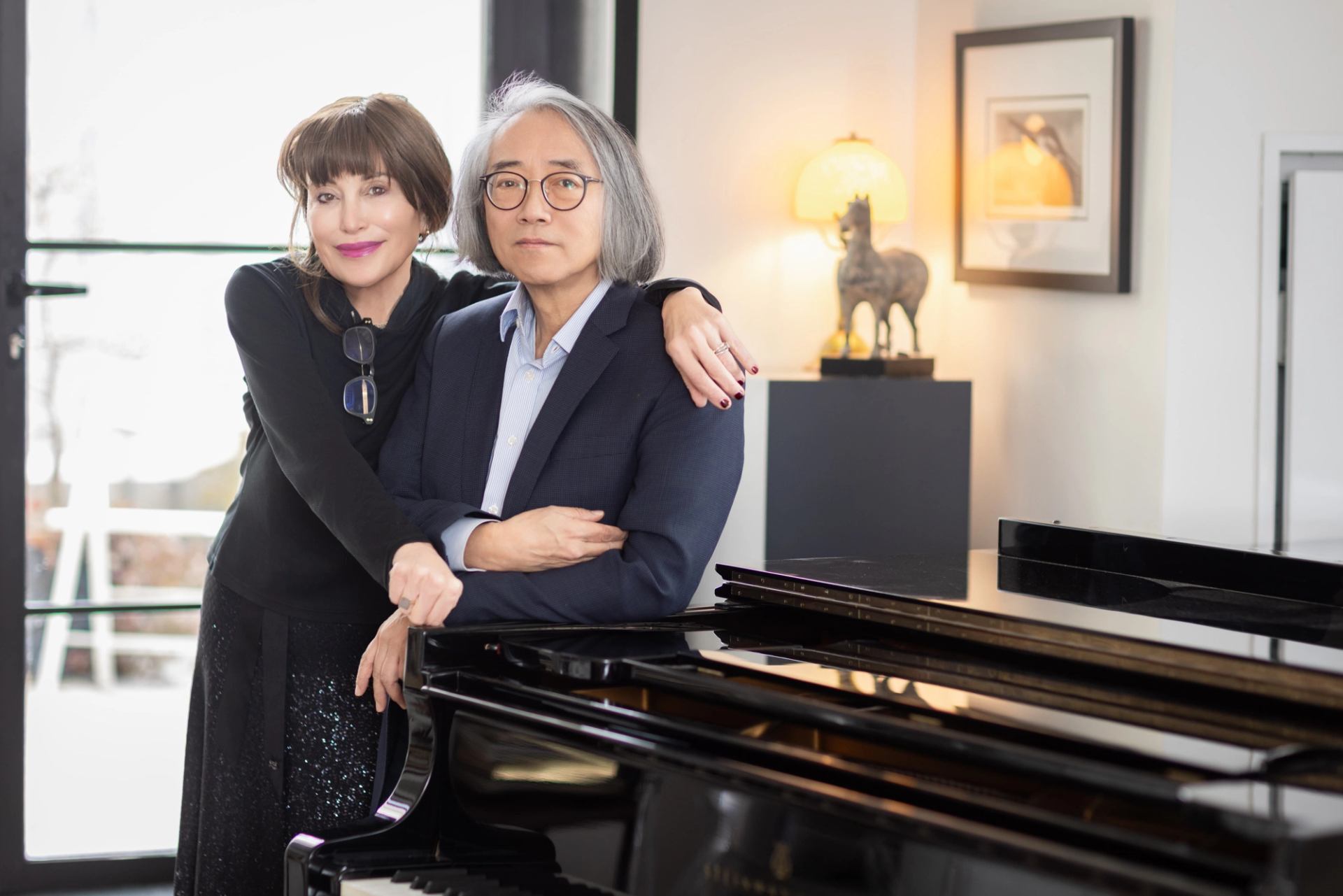 Two people stand beside a grand piano in a bright, modern living room.