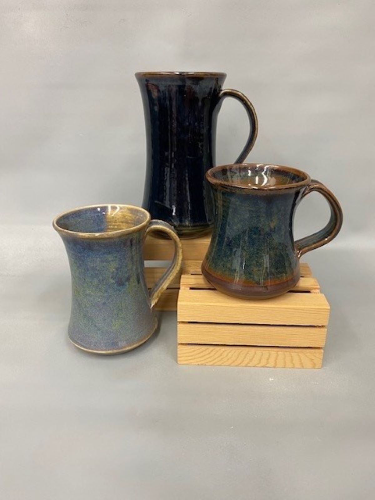Glazed ceramic mugs in blue and green sit on stacked wooden crates.
