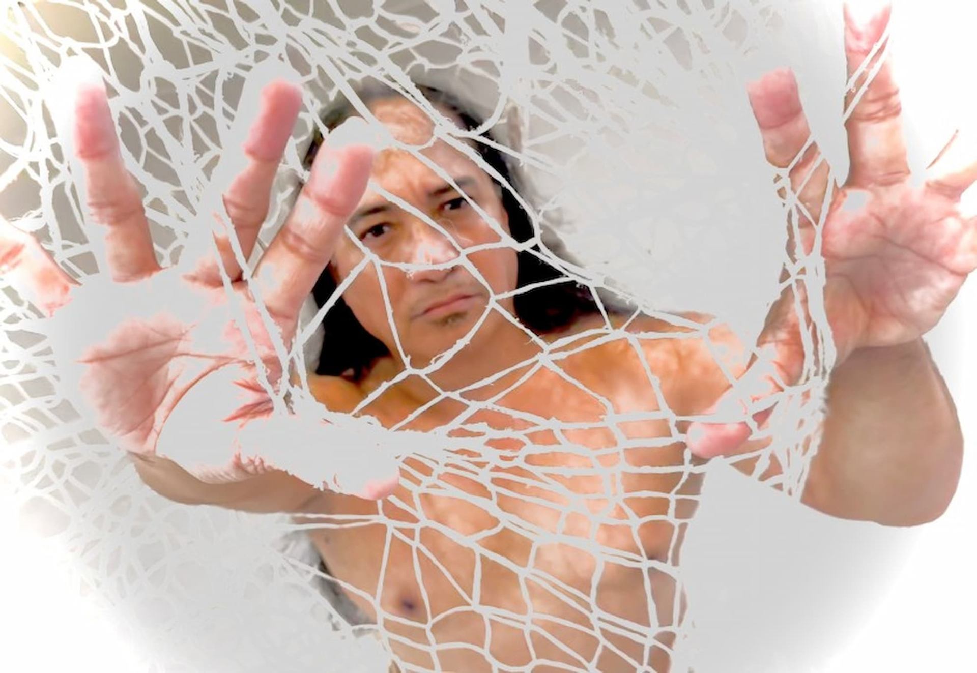 Shirtless person with long hair holds up a tangled white net toward the camera.