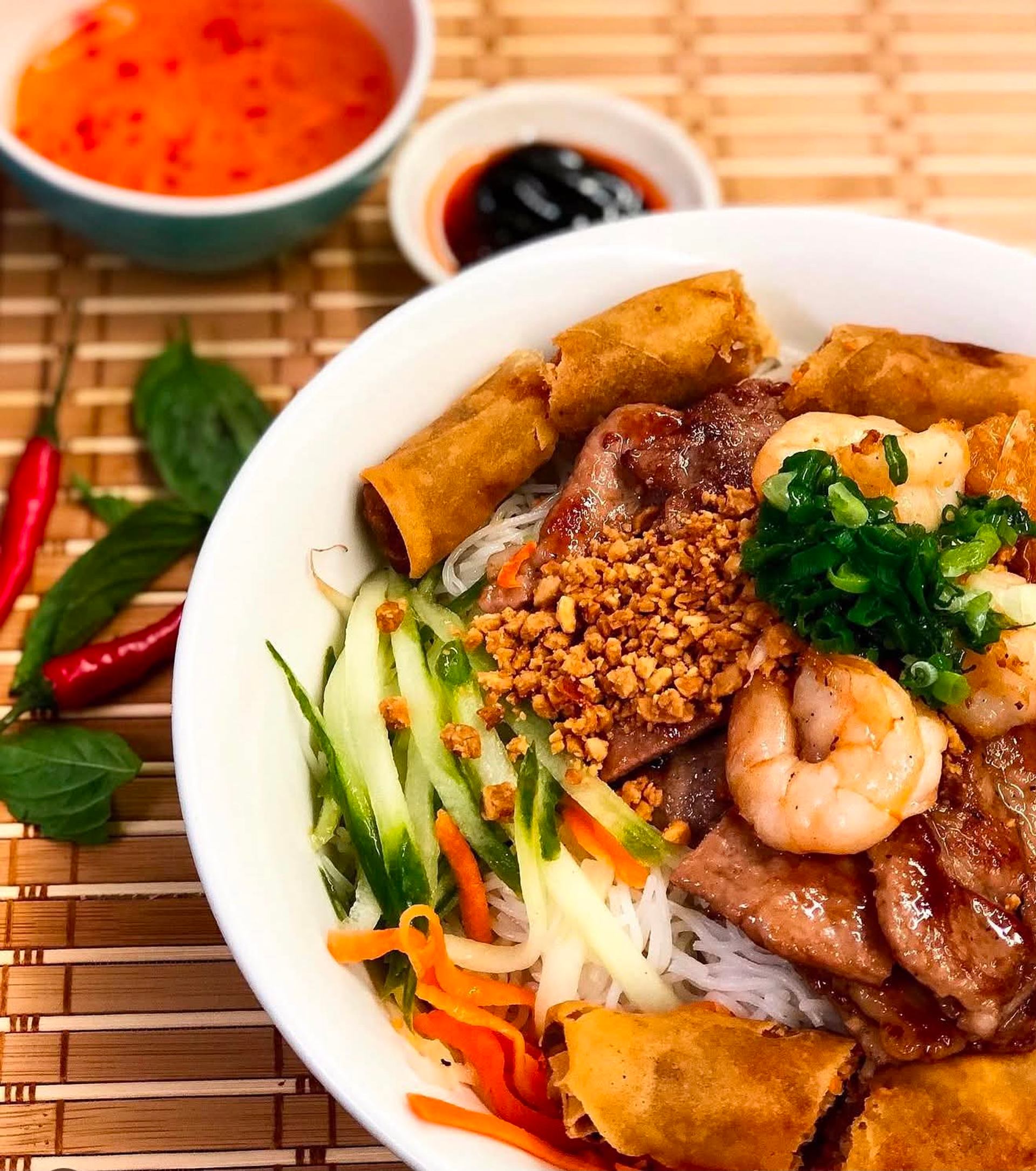 Bowl of vermicelli with grilled meat, shrimp, spring rolls and vegetables.