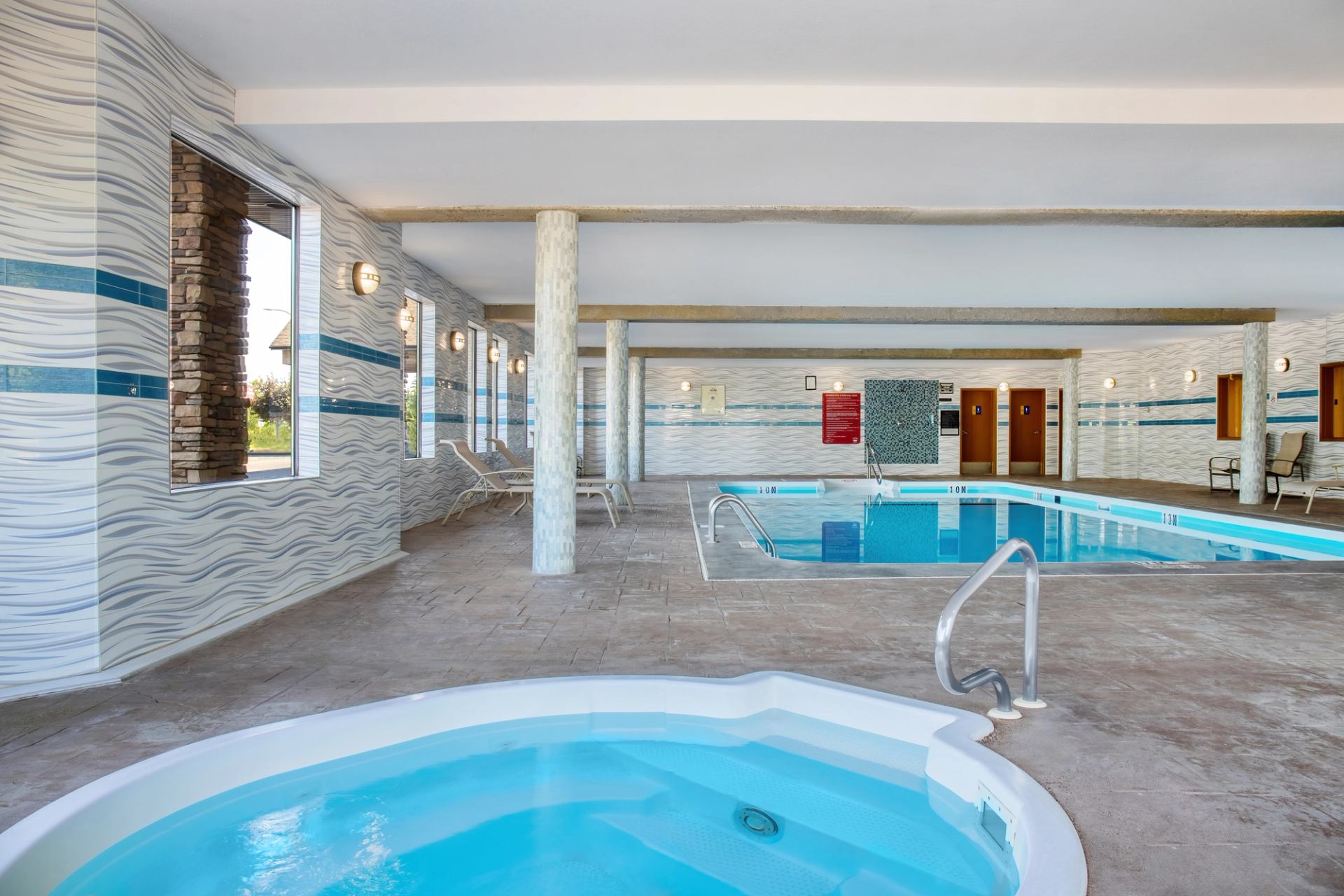 brightly lit pool area with hot tub and windows to the outside along the east wall