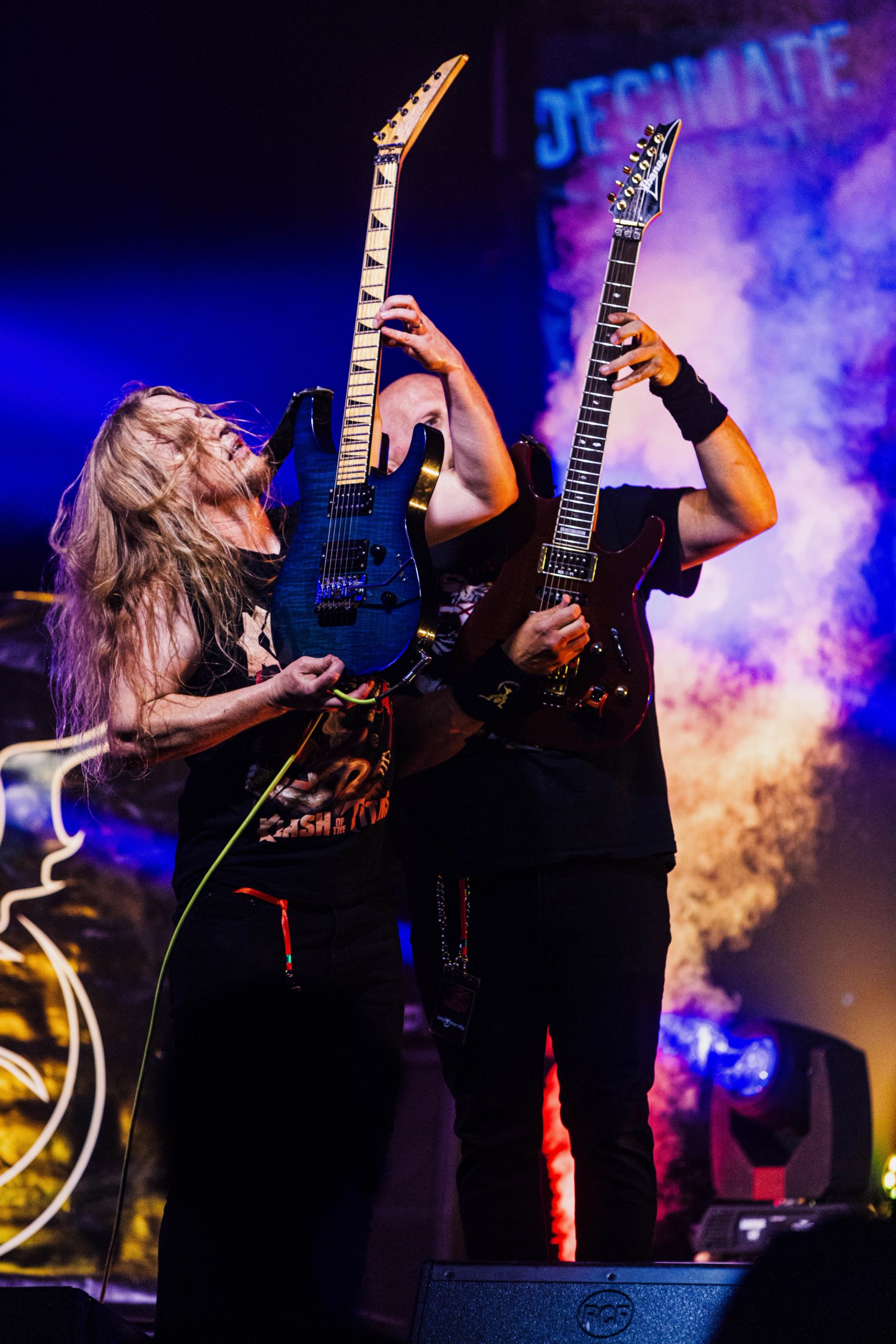 Decimate Metalfest shows two guitarists playing side by side on stage with dramatic lighting and smoke effects.
