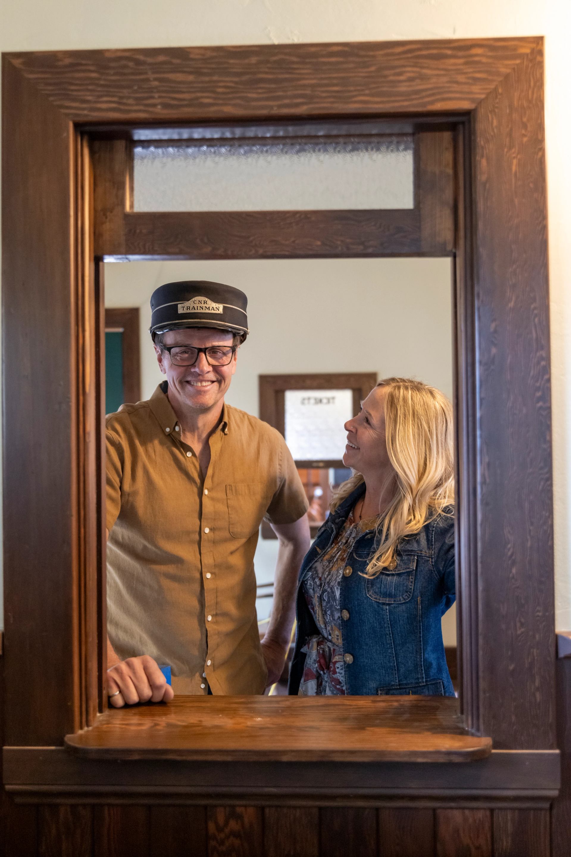 A woman poses next to a man in uniform at the Peace River Northern Alberta Railway Station.