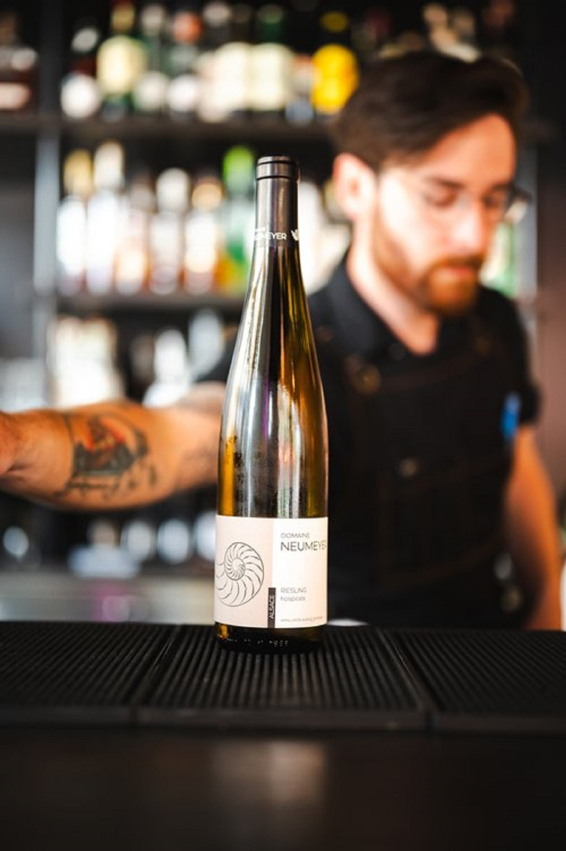 A sever at the bar with a bottle of wine sitting on the counter.