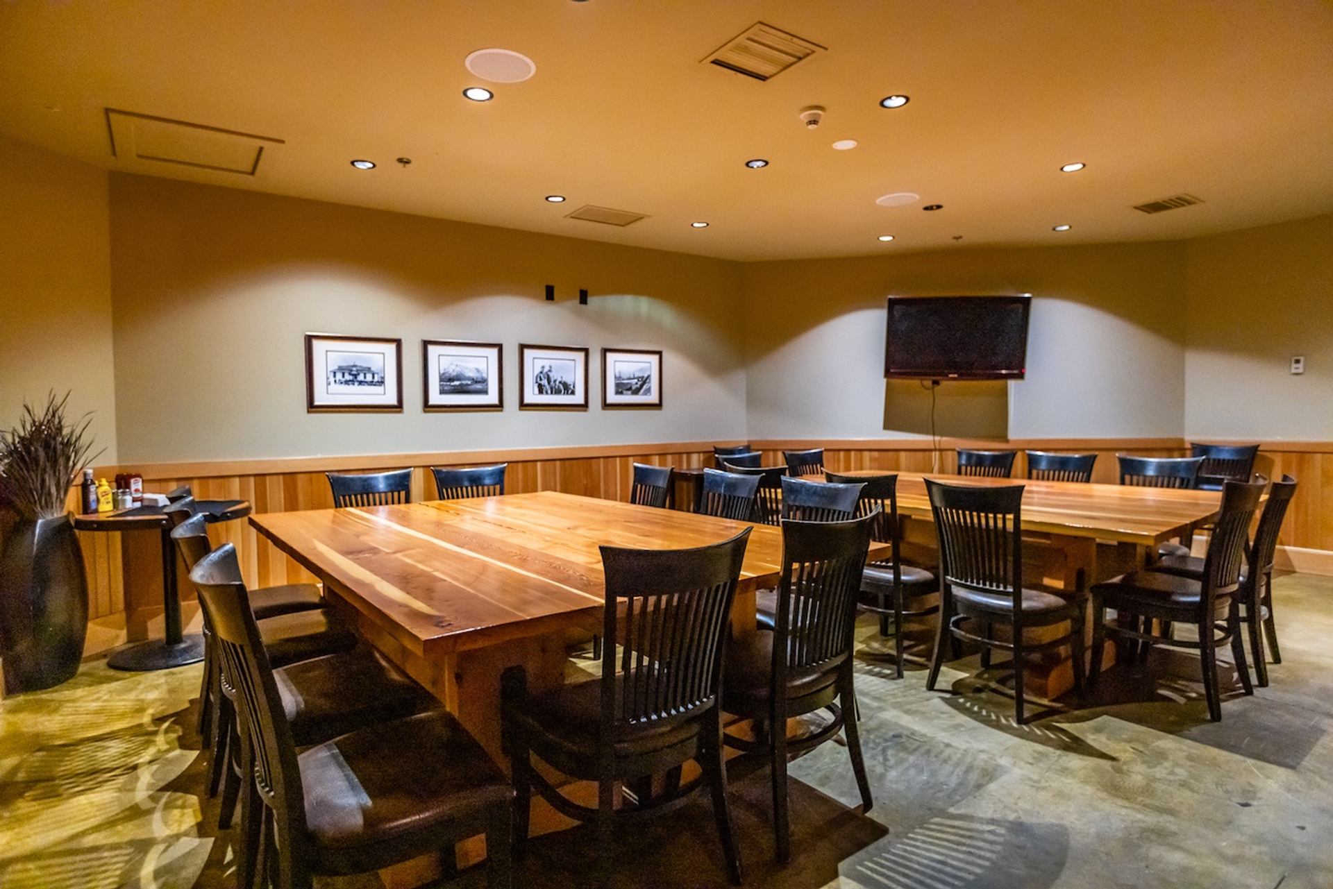 Cozy private room with long wooden tables, black chairs, and framed artwork on the walls.