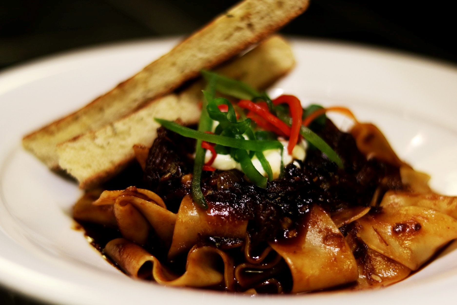Pasta dish with rich meat sauce, garnished with herbs and served with bread.