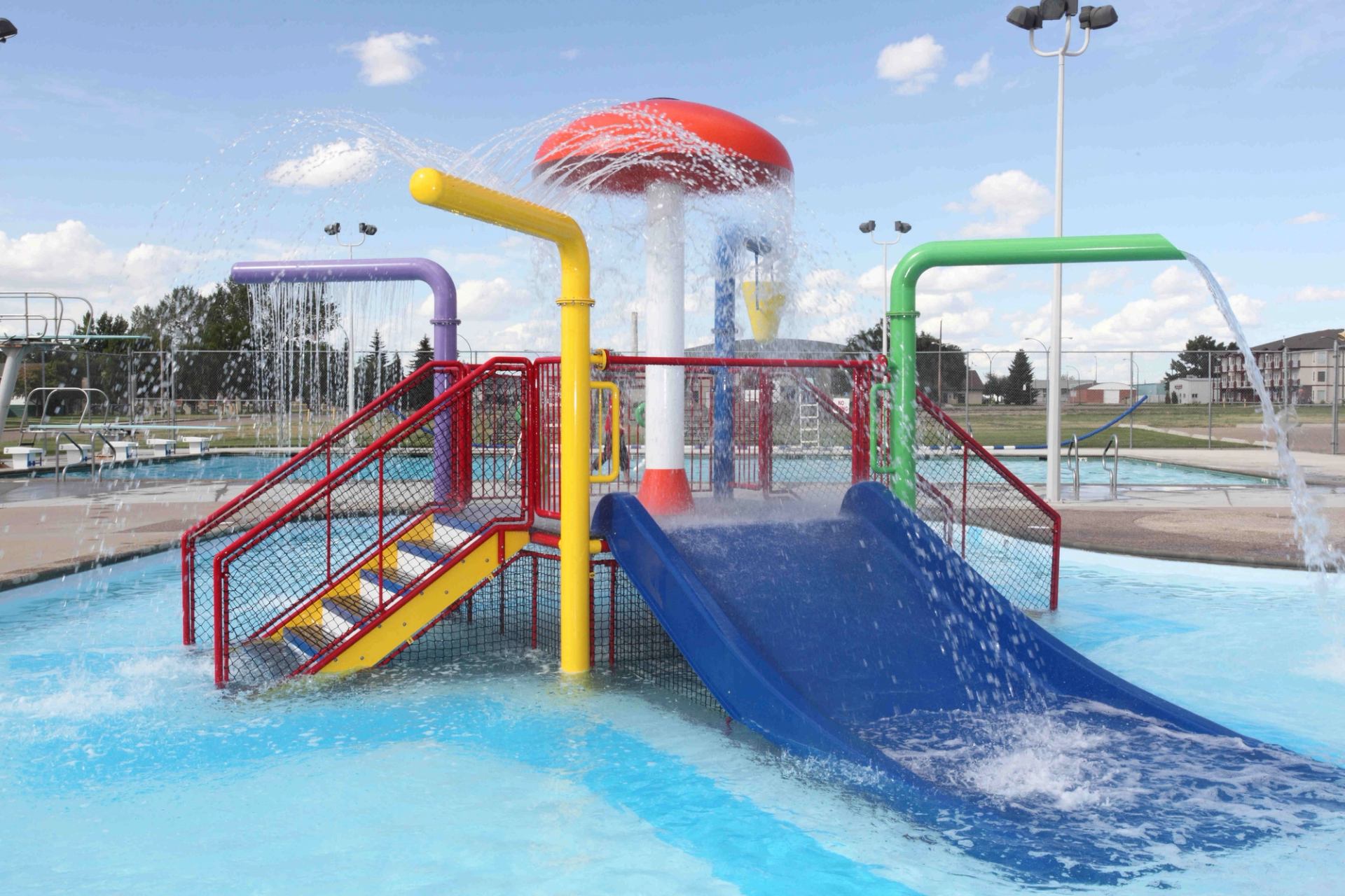 Outdoor water park slide and splash dome with colourful pipes and fountains in pool.