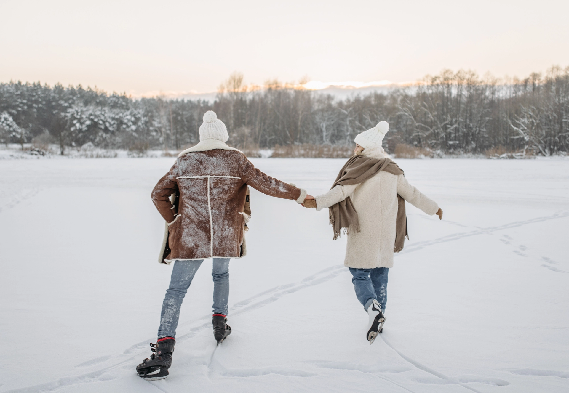 Two people holding hands while ice skating on a snowy frozen lake.