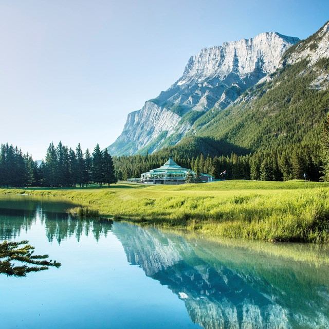 Fairmont Banff Springs Golf Course with reflective water, lush greens, and towering mountains.