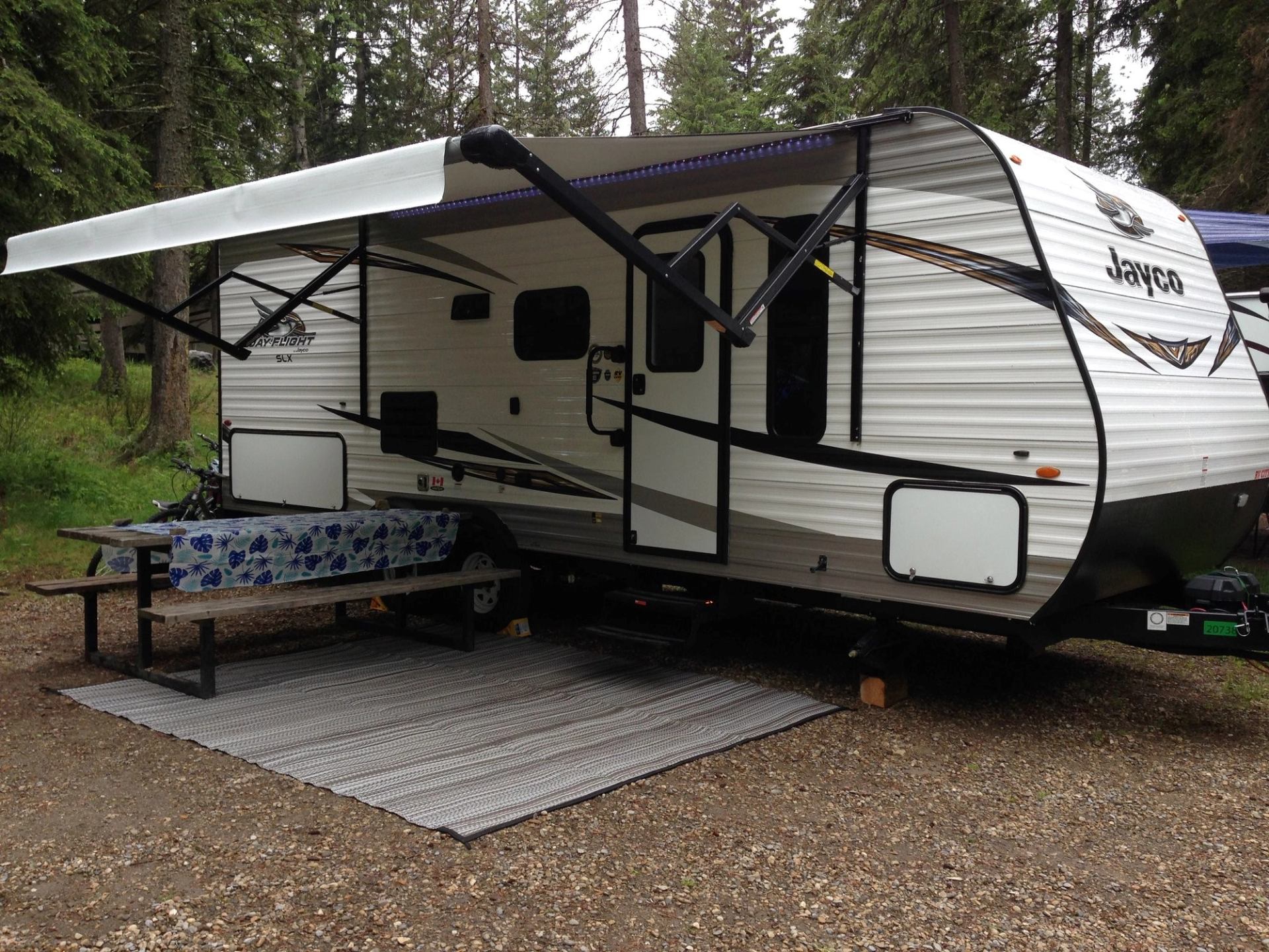 Camper trailer with awning and picnic table in a forest campsite.