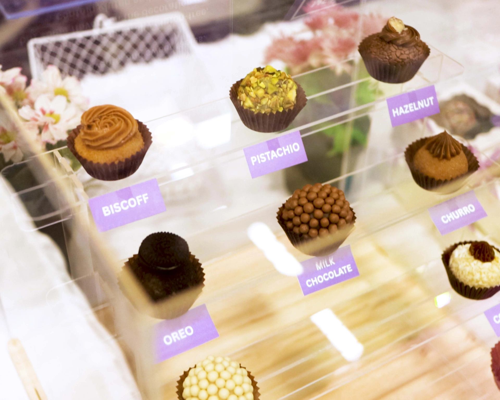 Display case with assorted labelled cupcakes, including Biscoff, pistachio, hazelnut and Oreo.
