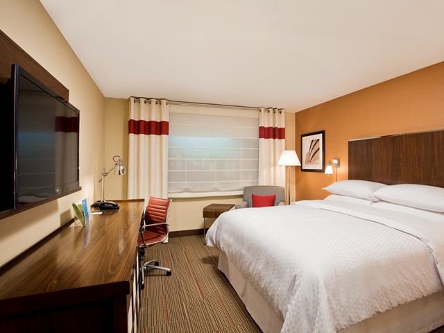 Hotel room with double bed, desk, chair, wall art, and bedside lamps.