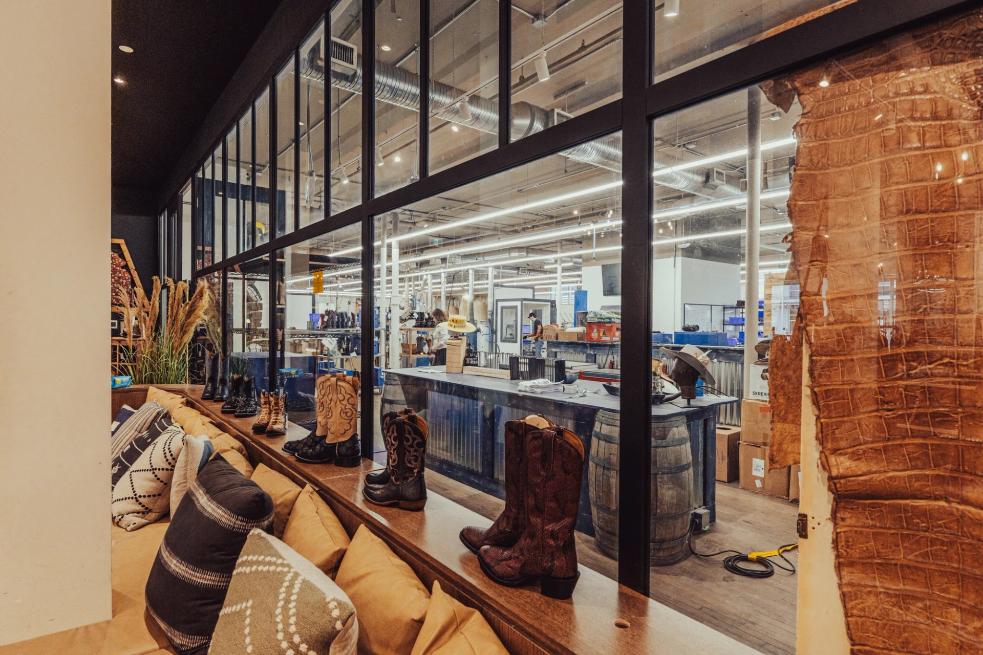 Display of cowboy boots beside cushions, overlooking workshop through large interior windows.