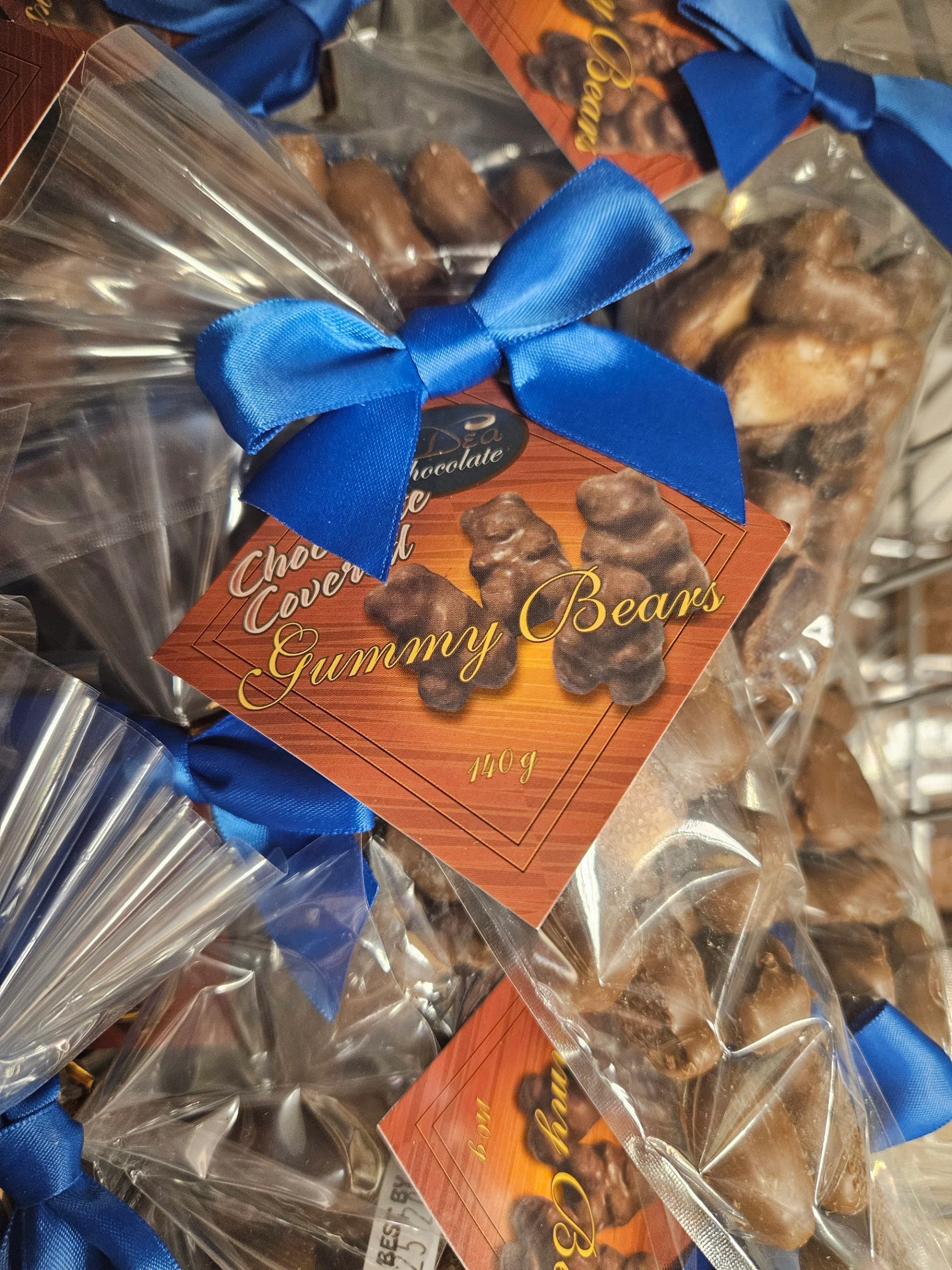 Clear bags of chocolate-covered gummy bears tied with blue ribbons and orange labels.