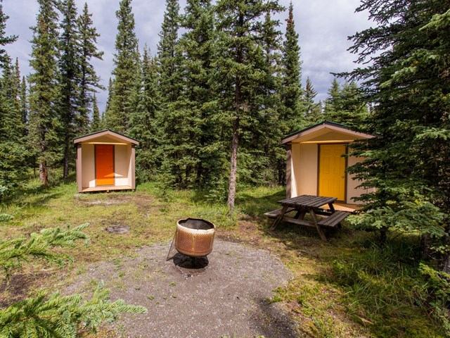 Two small cabins with colorful doors, a picnic table, and a fire pit in a forest setting.