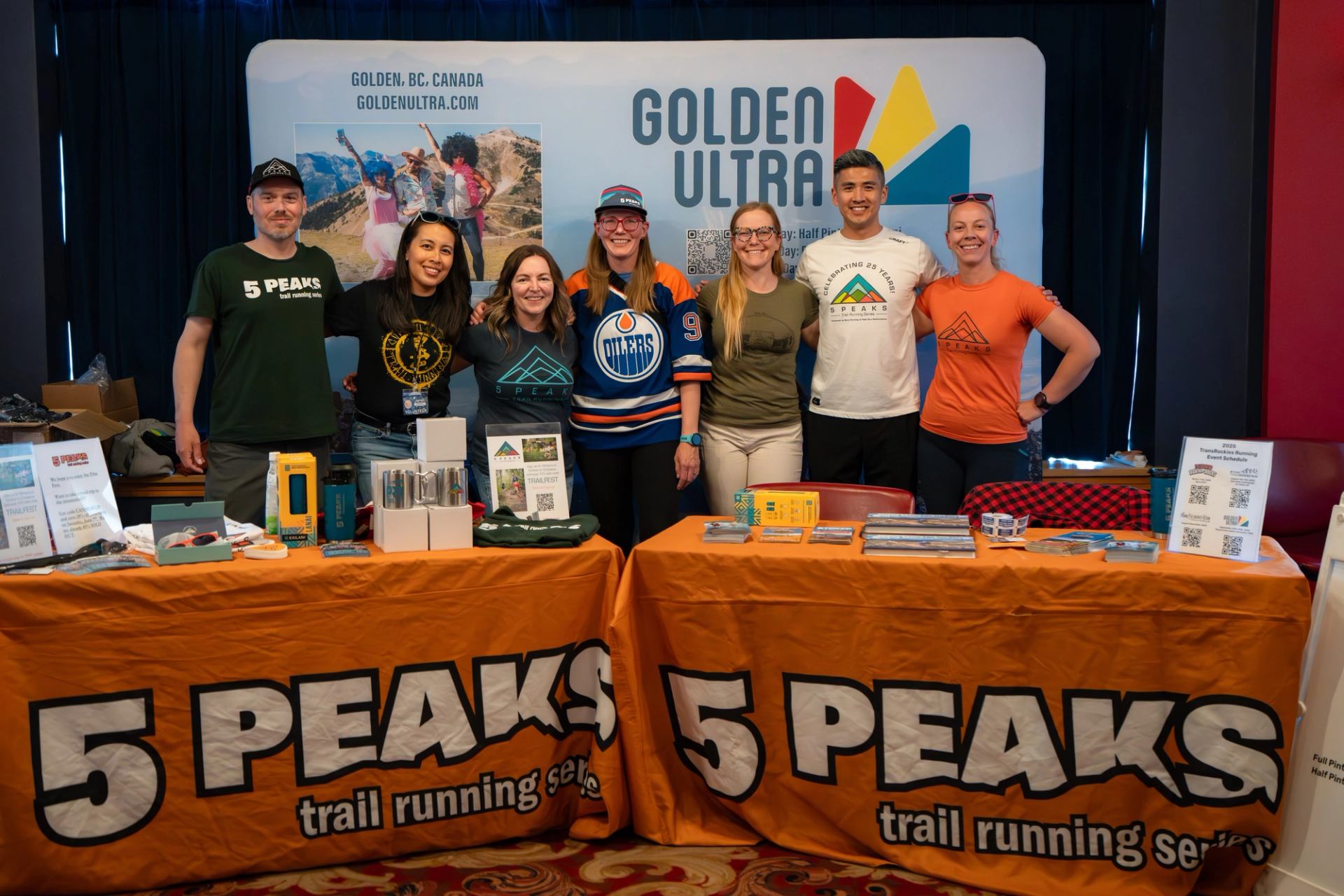 Group of people at 5 Peaks trail running booth with Golden Ultra banner behind.