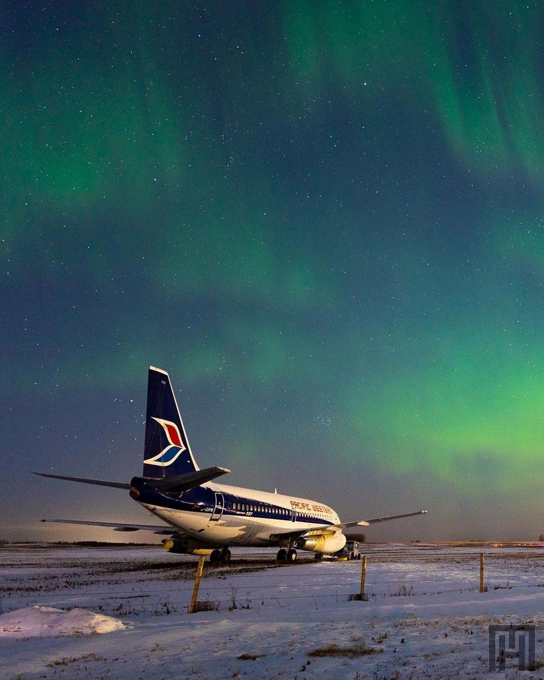 Rear photo of passenger airplane with northern lights glowing overhead.