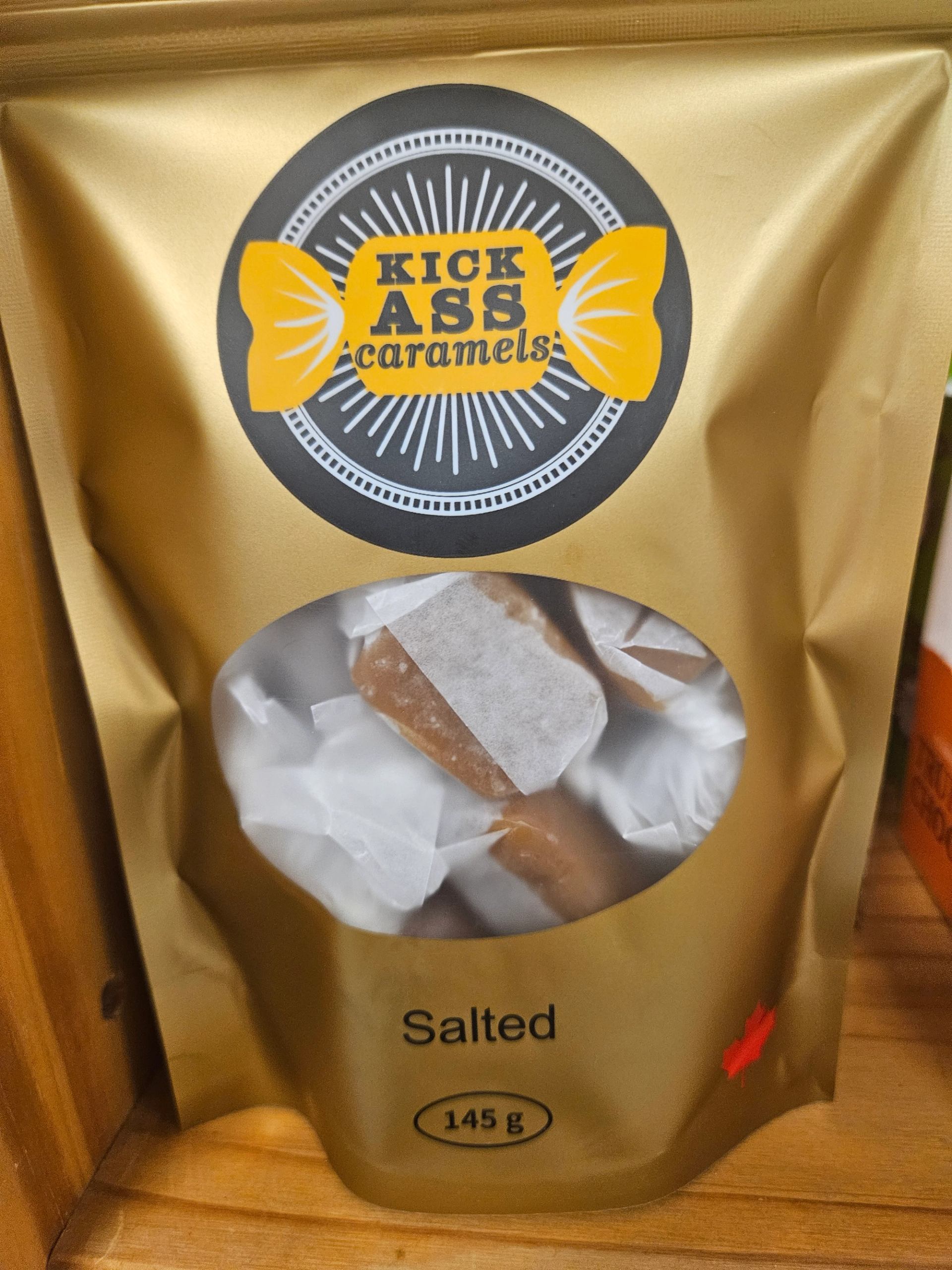 Gold bag of Kick Ass Salted Caramels with a clear window showing wrapped candies.